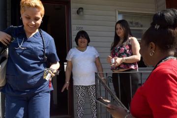 A Camden Coalition health practitioner leaving a house. Three individuals are standing around the house.