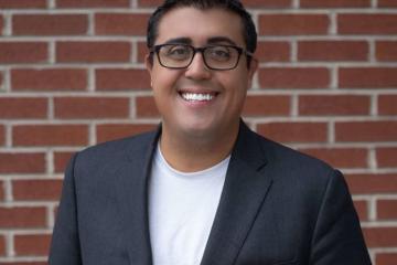 A headshot of AJ Gutierrez against a brick wall.