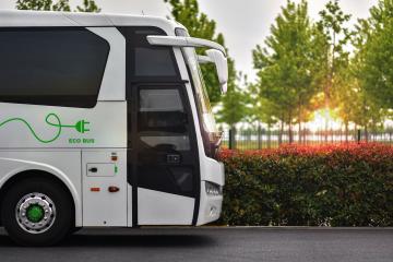 White electric shuttle bus drives down a tree-lined street at sunset