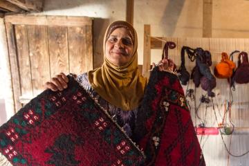 Woman wearing a headscarf holding up a rug
