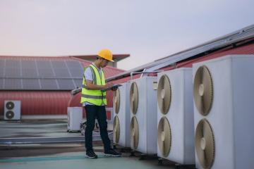 A man working, observing several heat pumps in a street